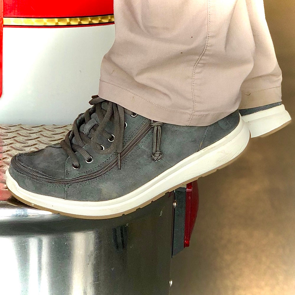 A person wearing light khaki pants and grey sneakers with white soles rests their foot on a shiny metal step.