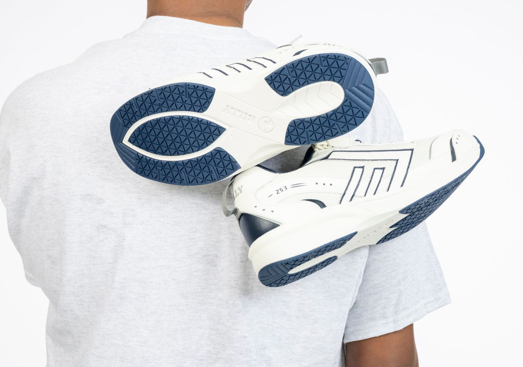 White sneakers with blue soles held by a person wearing a white shirt.