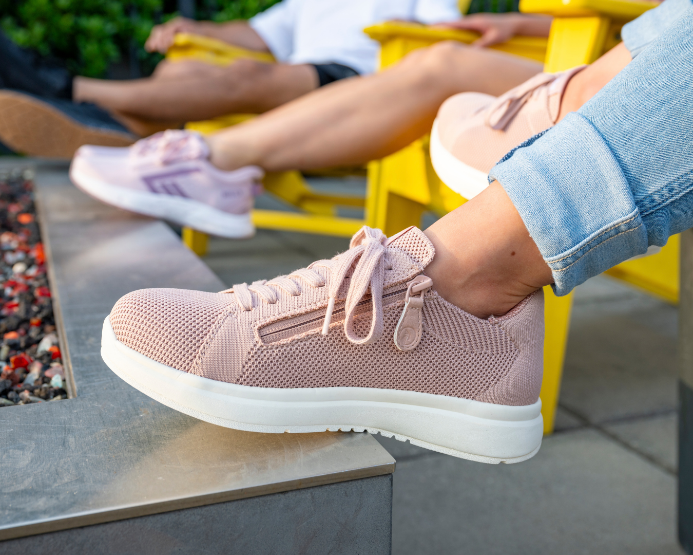 Two women and a man sitting around an outdoor firepit wearing BILLY shoes, including the Women’s Blush BILLY Comfort Knit, Women’s Mauve/White/Plum BILLY Sport Inclusion DZ1, and Men’s Black/Black/Gum BILLY Sport Inclusion DZ1.