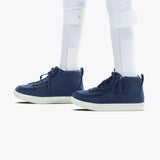 A close-up of a person wearing BILLY Footwear's Navy BILLY Classic D|R II High AFO-friendly sneakers with side zippers and white soles, along with white leg braces over white socks.