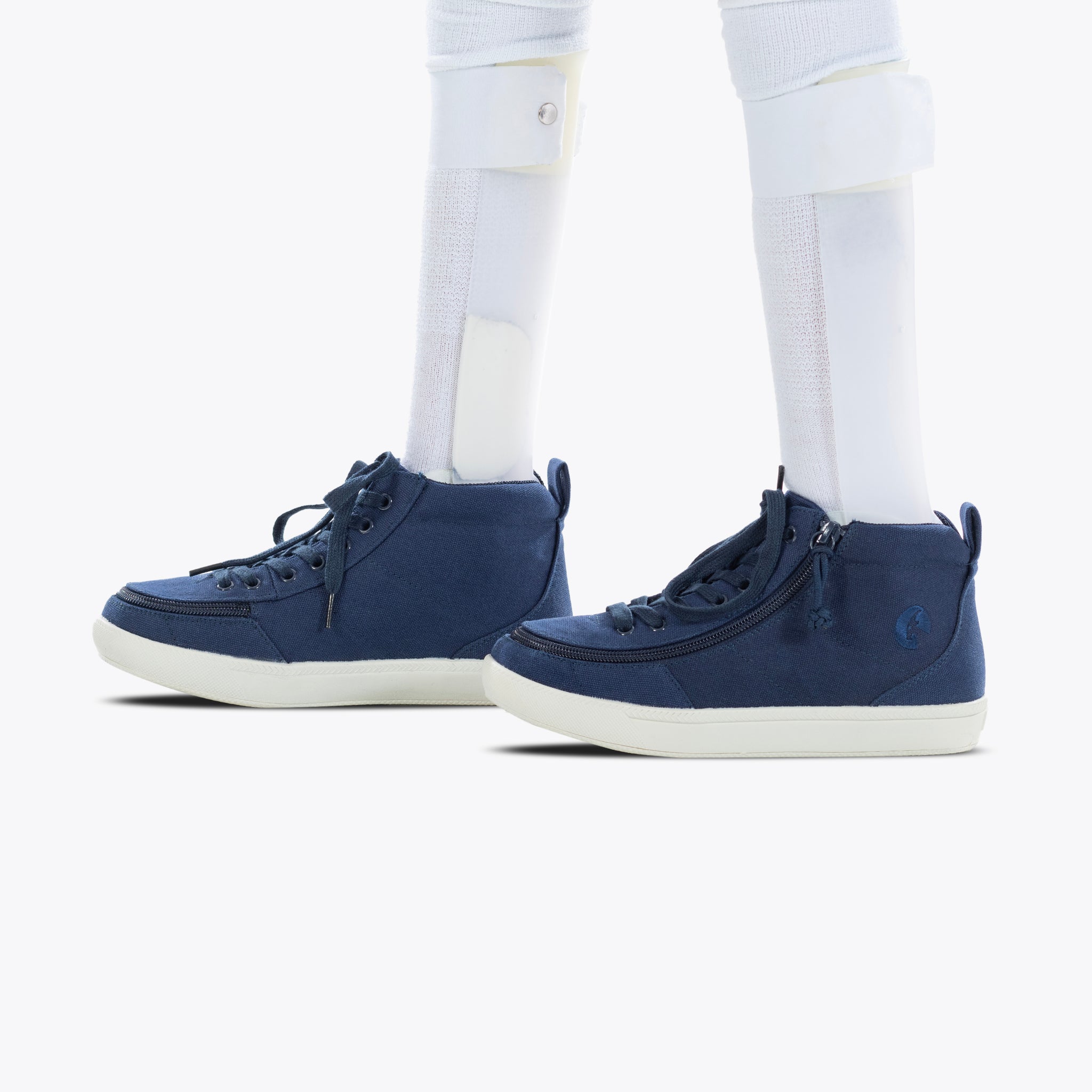 A close-up of a person wearing BILLY Footwear's Navy BILLY Classic D|R II High AFO-friendly sneakers with side zippers and white soles, along with white leg braces over white socks.