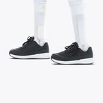 A person with prosthetic legs wears Black BILLY Goat orthotic shoes by BILLY Footwear, featuring white soles, standing on a plain white background.