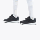 A person with prosthetic legs wears Black BILLY Goat orthotic shoes by BILLY Footwear, featuring white soles, standing on a plain white background.