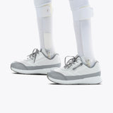 Close-up of two prosthetic legs fitted with SALE - White BILLY Goat shoes by BILLY Footwear, featuring an easy on-and-off zipper, standing on a white background.