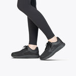 A person wearing Black to the Floor BILLY Sport Inclusion shoes from BILLY Footwear and black leggings stands on a light gray background, with only their legs and feet visible.