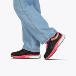 A person in light blue jeans and BILLY Footwear's SALE - Black/Fuchsia Fire BILLY Sport Inclusion shoes walks with one foot lifted and the other flat, set against a plain white background.