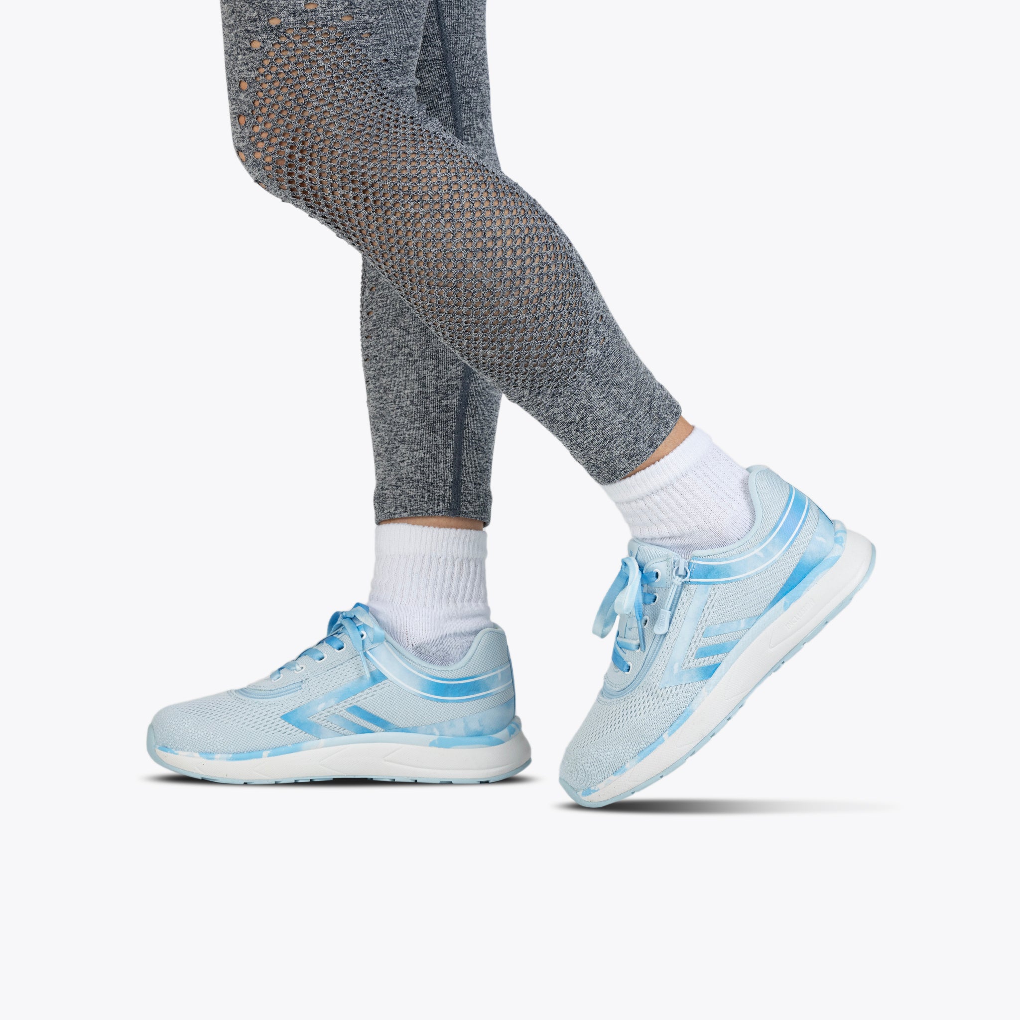 A person wearing gray textured leggings, white socks, and SALE - Sky Blue BILLY Sport Inclusion shoes by BILLY Footwear stands with one foot slightly raised on a plain white background.