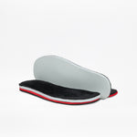 Two shoe insoles from the Black BILLY Ice Boot by BILLY Footwear have black plush tops, white midsoles, and red accents. One insole lies flat, while the other shows its plain light gray underside propped behind it.