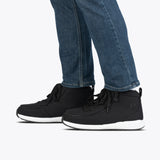 A person wearing blue jeans and BILLY Footwear Men's Black/White BILLY Goat Classic High sneakers with black laces and white soles, standing on a white background. These shoes are ideal for use with orthotics and have a simple, casual design.
