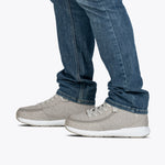 A person wearing blue jeans and light gray Men's Grey Jersey BILLY Goat Classic High shoes by BILLY Footwear, featuring white soles and an adjustable fit, stands on a white background.