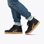 Person wearing cuffed blue jeans and BILLY Footwear Men's Black/Gum BILLY CS High sneakers, featuring tan soles and geometric tan designs, stands with one foot in front of the other on a plain white background.