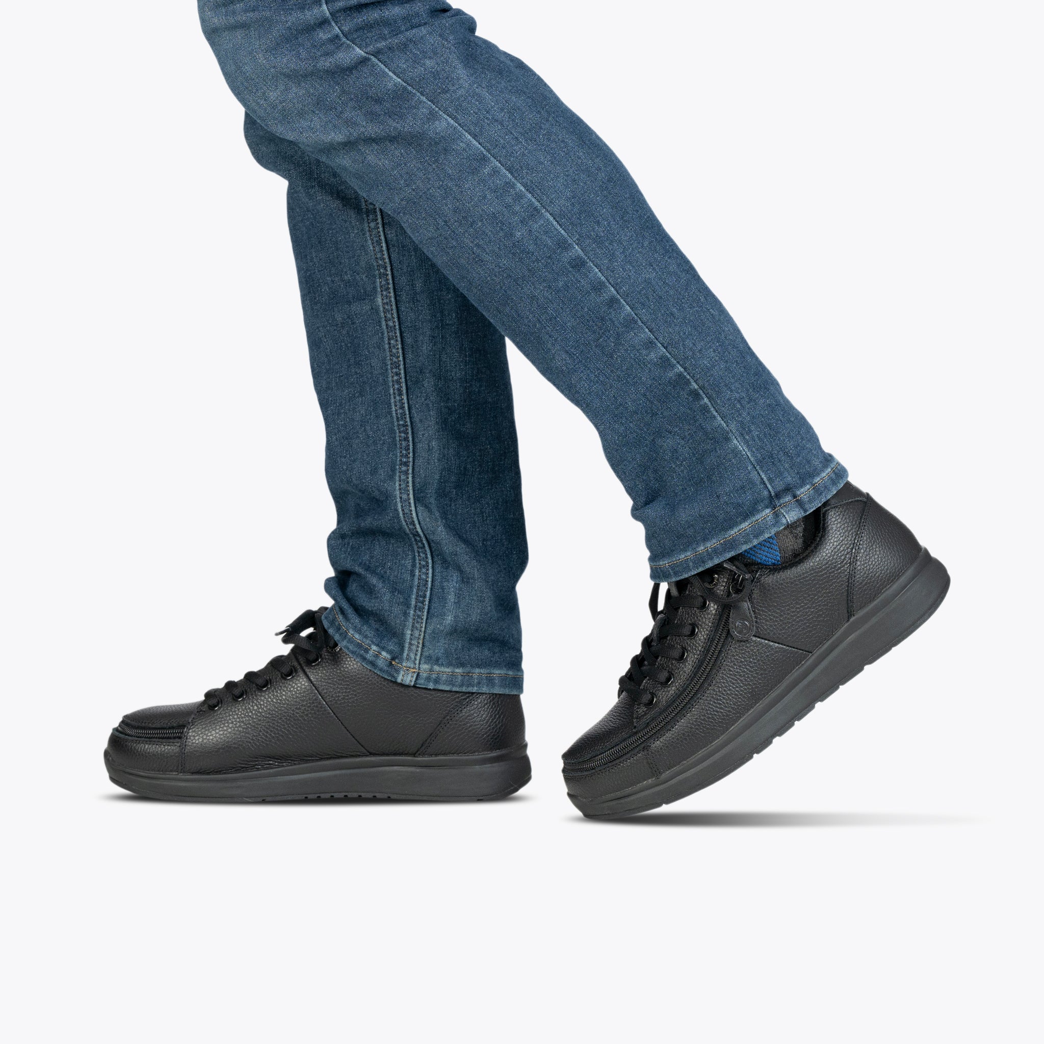 A person in blue jeans steps forward wearing BILLY Footwear Men's Black to the Floor Leather Comfort Plush shoes, set against a plain light background.