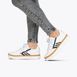 A person in acid-wash skinny jeans and BILLY Footwear Women's White/Black BILLY CS Low sensory-friendly double zipper sneakers with white soles walks on a light gray background.