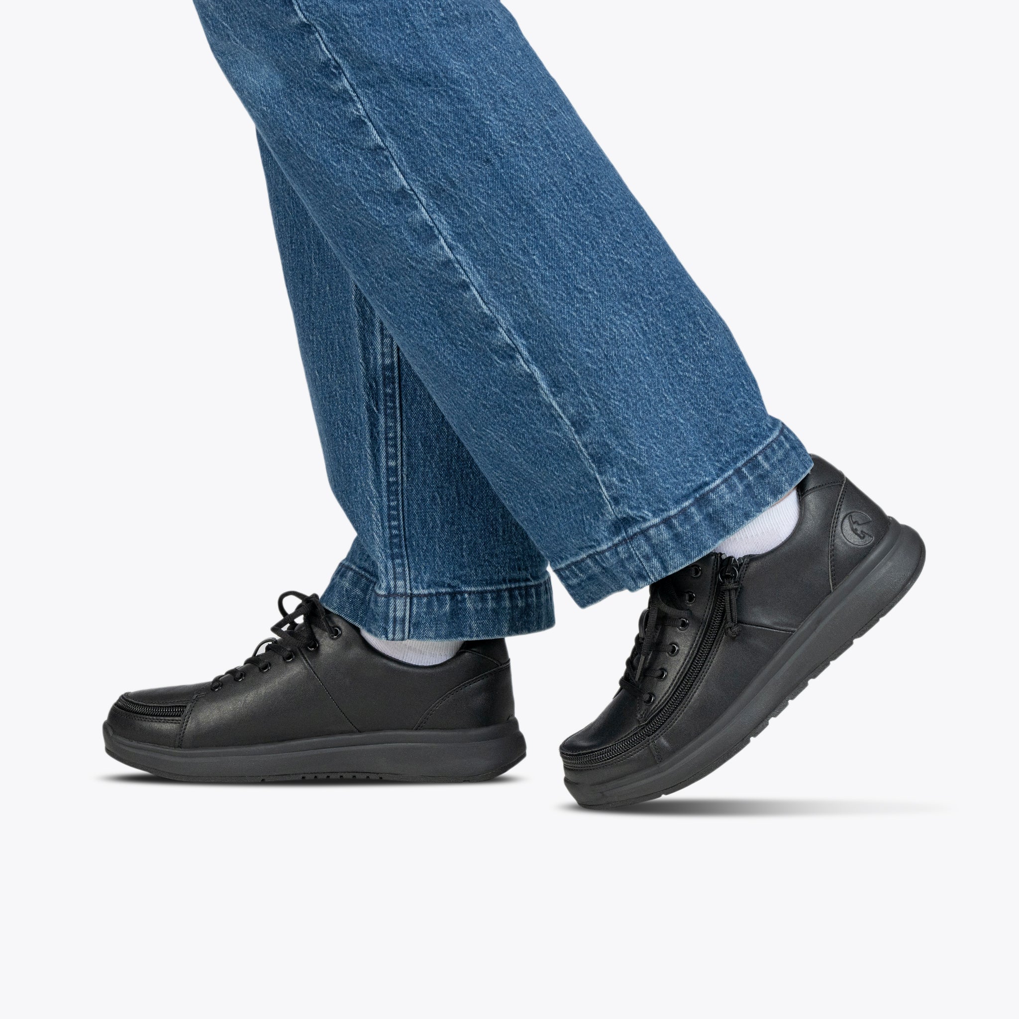 Person walking in blue jeans and black sneakers, shown from the knees down