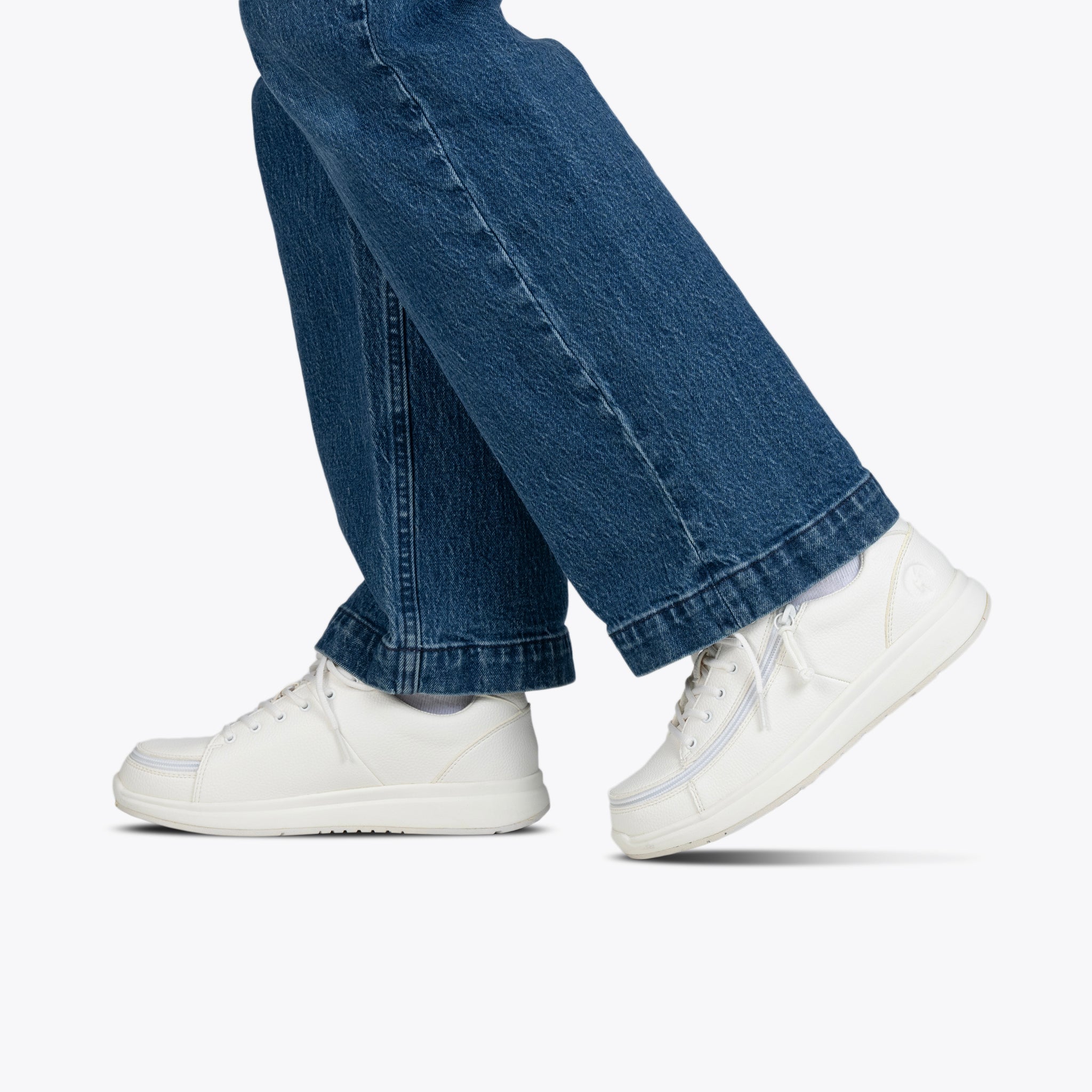 Person walking in blue jeans and white sneakers, shown from the knees down