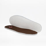 A pair of Women's Chestnut BILLY Cozy II insoles by BILLY Footwear is shown: one lies flat displaying its brown top with logo, while the other stands to reveal a white underside with blue speckles, set against a white background.