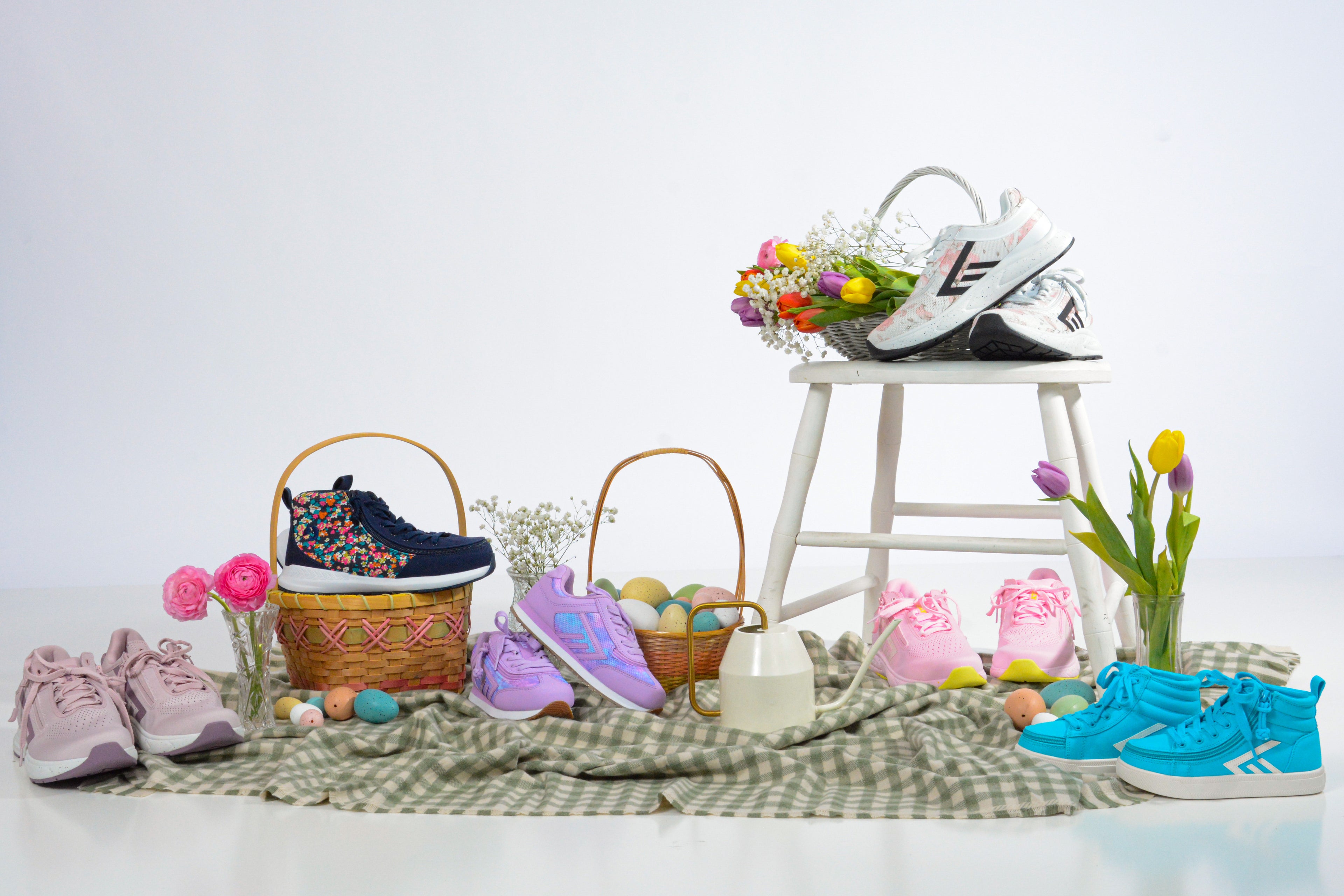 Colorful children's shoes, women's shoes, and accessories on a checkered blanket with a white stool and flowers.