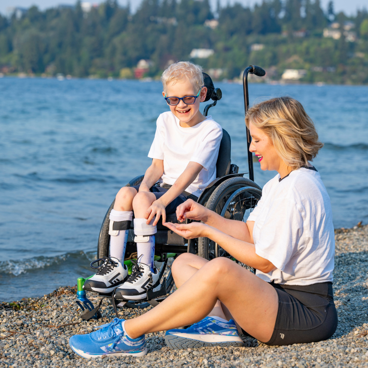Woman assisting a child in a wheelchair by a lake