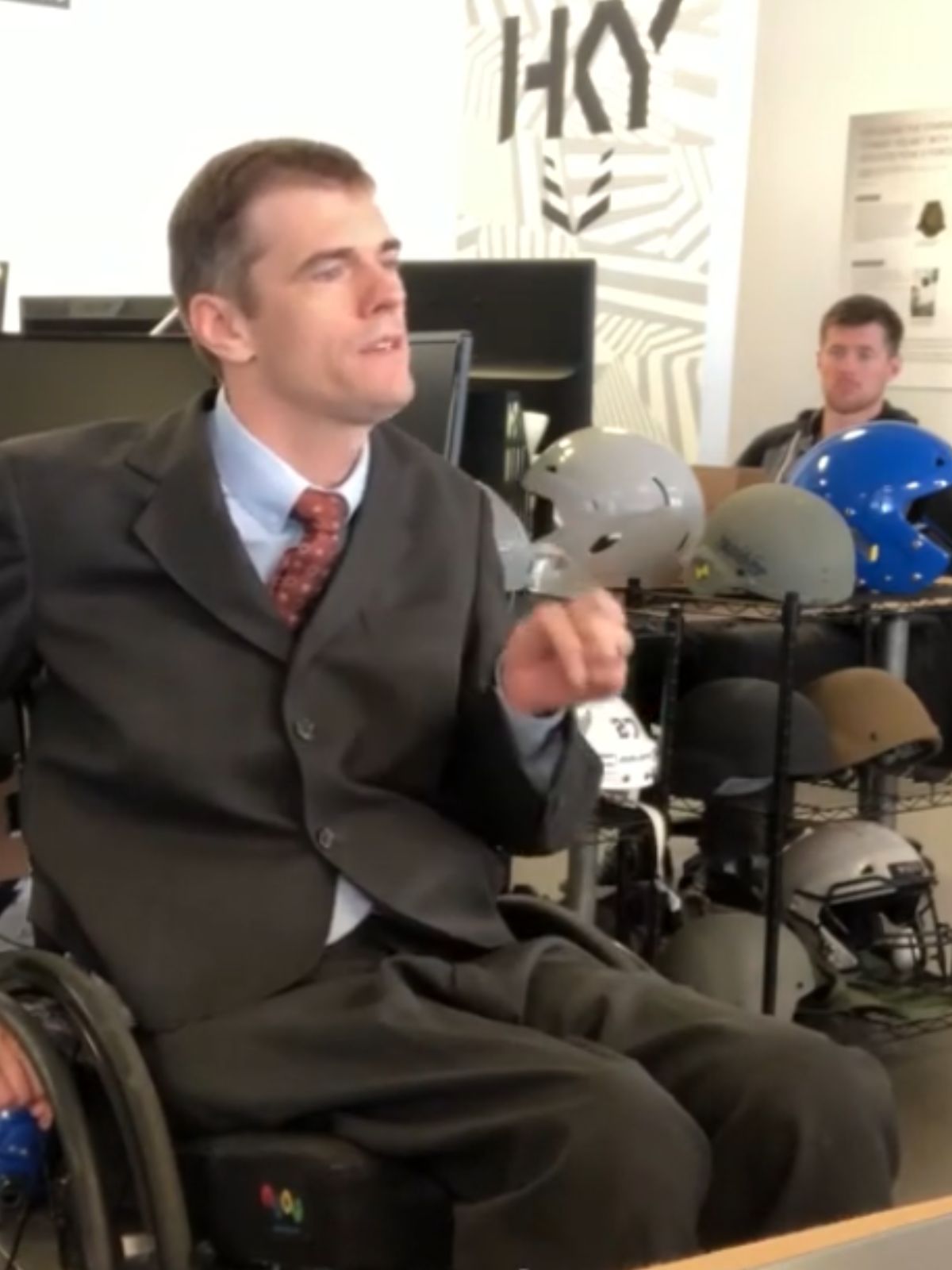Man in a suit sitting in an office chair with colleagues in the background